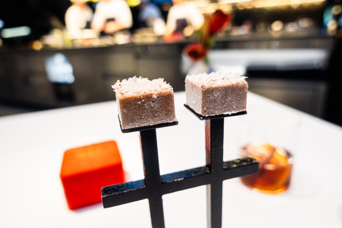 Sweets on a black stand: a pale square and a chocolate square with gold leaf.